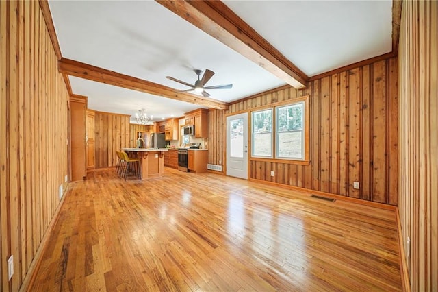 unfurnished living room featuring beamed ceiling, ceiling fan with notable chandelier, light hardwood / wood-style floors, and wood walls