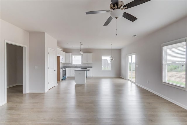 unfurnished living room with ceiling fan, plenty of natural light, sink, and light hardwood / wood-style flooring