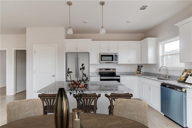 kitchen with a center island, white cabinets, light stone countertops, decorative light fixtures, and stainless steel appliances