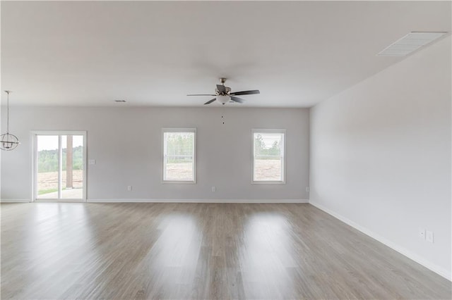 empty room with a healthy amount of sunlight, ceiling fan with notable chandelier, and light hardwood / wood-style floors