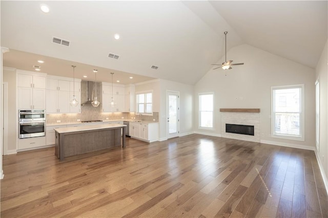 kitchen featuring wall chimney exhaust hood, white cabinetry, decorative light fixtures, a center island, and stainless steel appliances