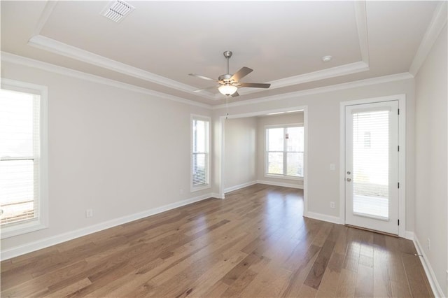 empty room with a raised ceiling, wood-type flooring, and ornamental molding