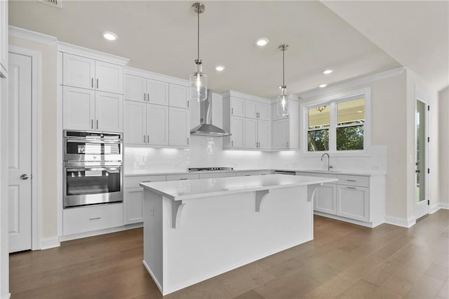 kitchen with white cabinets, a kitchen island, hanging light fixtures, and wall chimney exhaust hood