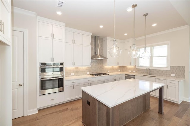 kitchen featuring sink, wall chimney range hood, a kitchen island, stainless steel appliances, and white cabinets