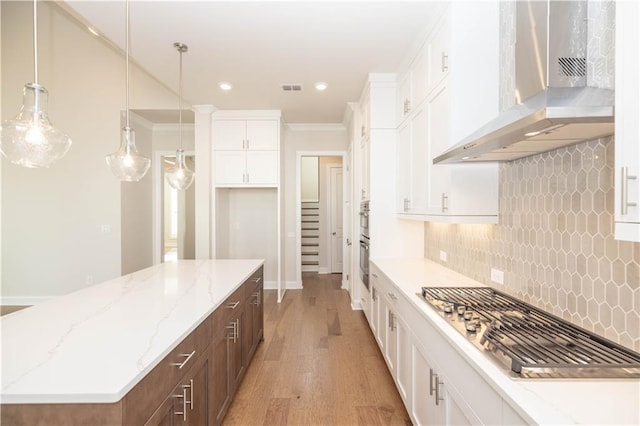 kitchen with appliances with stainless steel finishes, wall chimney exhaust hood, ornamental molding, and white cabinets