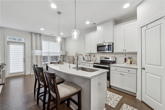 kitchen with stainless steel appliances, light countertops, hanging light fixtures, white cabinetry, and a sink