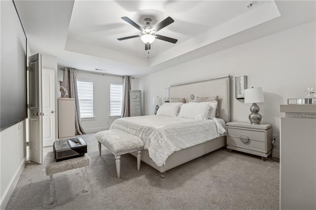 bedroom with baseboards, a tray ceiling, a ceiling fan, and light colored carpet