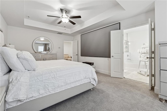 bedroom featuring visible vents, baseboards, light colored carpet, ensuite bath, and a tray ceiling