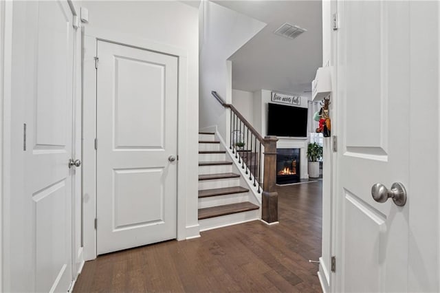 foyer with dark wood-style floors, a glass covered fireplace, visible vents, and stairs