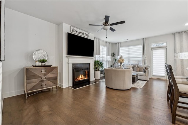 living area featuring dark wood-style floors, ceiling fan, baseboards, and a glass covered fireplace