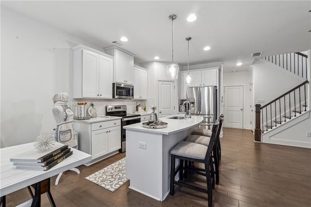 kitchen with stainless steel appliances, white cabinets, hanging light fixtures, light countertops, and an island with sink