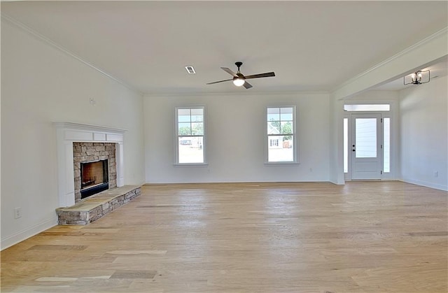 unfurnished living room with ceiling fan with notable chandelier, light hardwood / wood-style floors, a stone fireplace, and ornamental molding