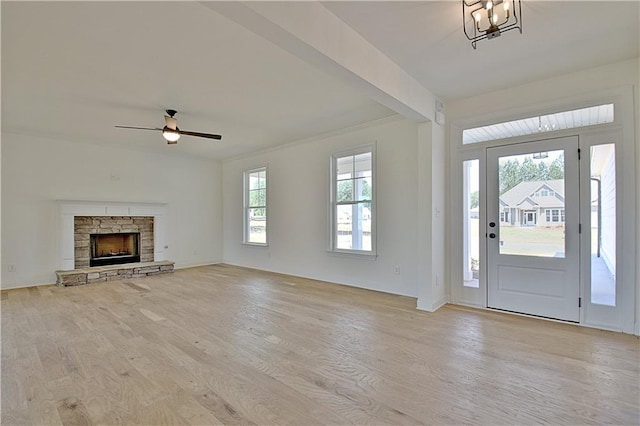 entrance foyer with a stone fireplace, light hardwood / wood-style floors, ceiling fan with notable chandelier, and ornamental molding