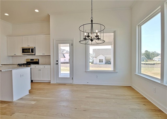 kitchen with tasteful backsplash, stainless steel appliances, pendant lighting, a notable chandelier, and white cabinets