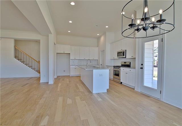 kitchen with white cabinets, light stone countertops, stainless steel appliances, and a kitchen island with sink