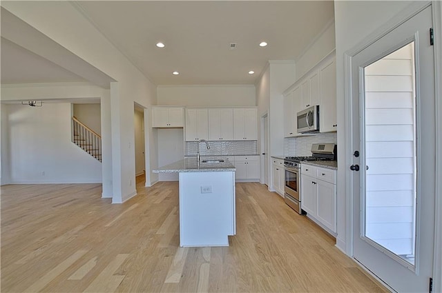 kitchen featuring light stone countertops, tasteful backsplash, stainless steel appliances, white cabinetry, and an island with sink