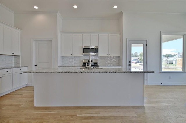 kitchen featuring white cabinets, light stone countertops, an island with sink, and stainless steel appliances