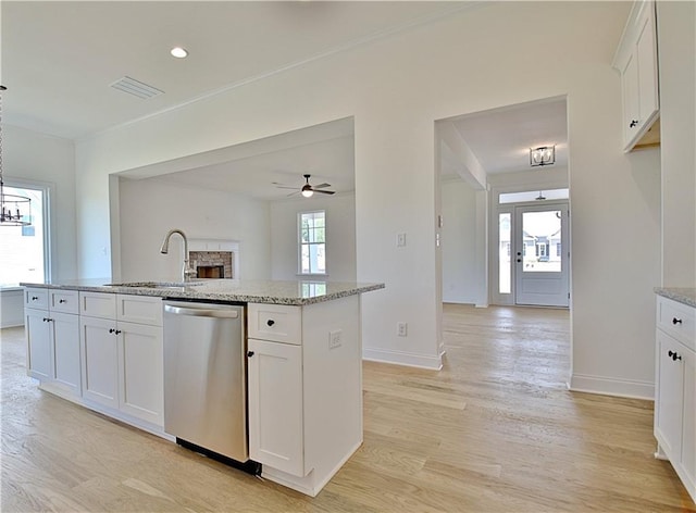 kitchen with a kitchen island with sink, ceiling fan with notable chandelier, sink, stainless steel dishwasher, and white cabinetry