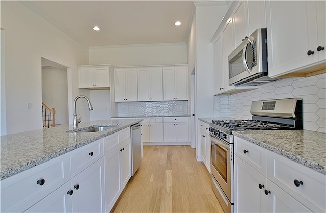 kitchen with light stone countertops, appliances with stainless steel finishes, sink, white cabinets, and light hardwood / wood-style floors