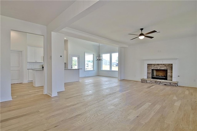 unfurnished living room with ceiling fan with notable chandelier, light wood-type flooring, and a fireplace