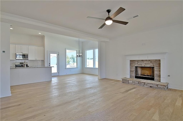 unfurnished living room with a stone fireplace, light hardwood / wood-style floors, ceiling fan with notable chandelier, and ornamental molding