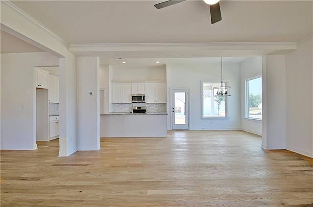 unfurnished living room with ceiling fan with notable chandelier, light wood-type flooring, and crown molding