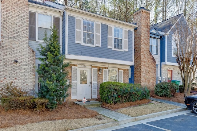 townhome / multi-family property with uncovered parking, brick siding, and a chimney