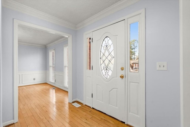 foyer featuring light wood-type flooring, ornamental molding, and a textured ceiling