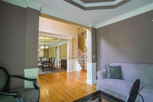 sitting room with an inviting chandelier, crown molding, wood-type flooring, and a raised ceiling