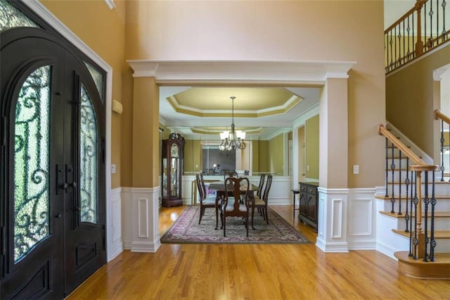 entrance foyer with an inviting chandelier, a tray ceiling, ornamental molding, light hardwood / wood-style floors, and french doors