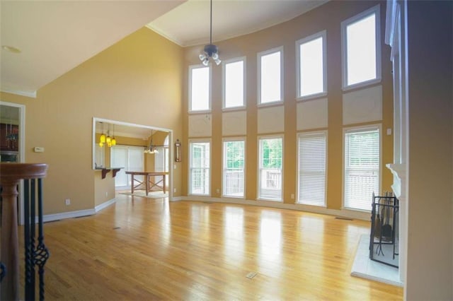 unfurnished living room featuring crown molding, a towering ceiling, light hardwood / wood-style flooring, and a chandelier