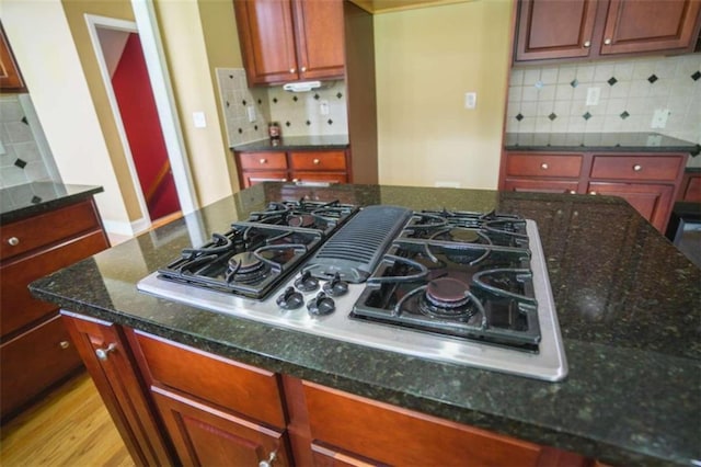 kitchen with stainless steel gas cooktop, light wood-type flooring, dark stone counters, and backsplash