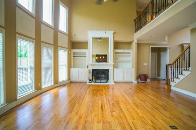 unfurnished living room with ceiling fan, a high ceiling, and light wood-type flooring