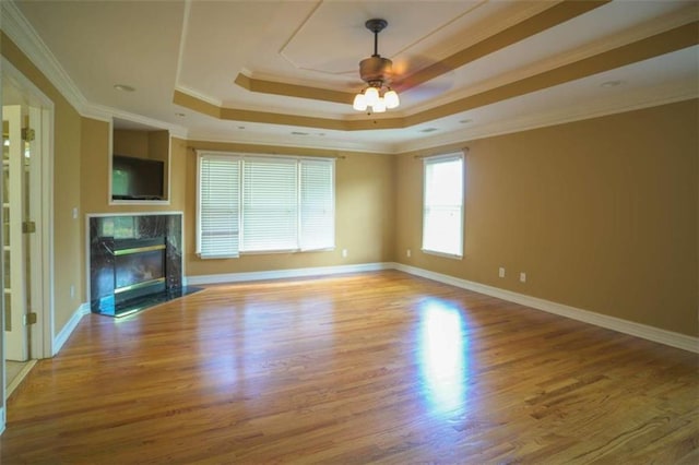 unfurnished living room featuring light wood-type flooring, a tray ceiling, a high end fireplace, ceiling fan, and crown molding