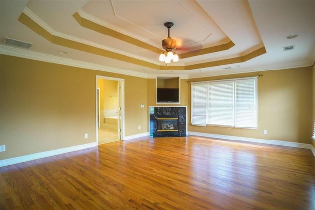 unfurnished living room with a premium fireplace, crown molding, hardwood / wood-style flooring, and a tray ceiling