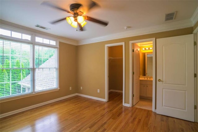 unfurnished bedroom featuring ceiling fan, multiple windows, a walk in closet, and ensuite bath