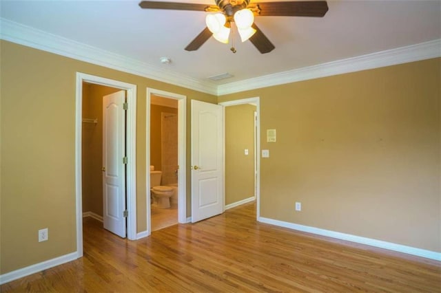 unfurnished bedroom featuring ceiling fan, light wood-type flooring, ornamental molding, a walk in closet, and ensuite bath