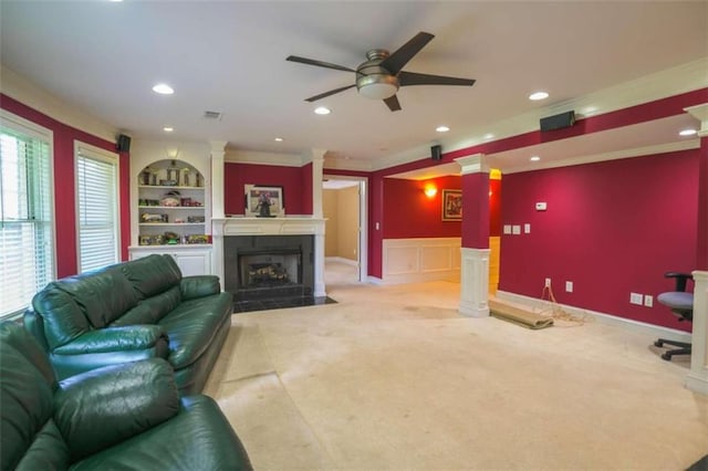 carpeted living room featuring ornate columns, ceiling fan, crown molding, and built in features