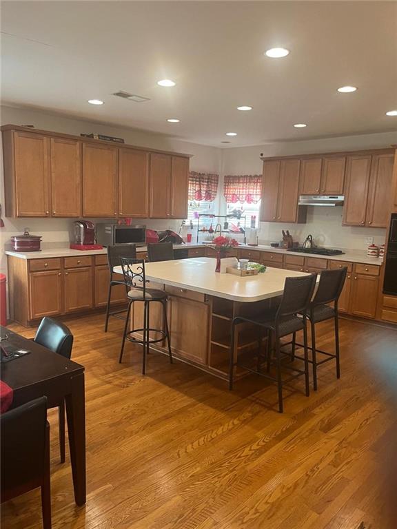947 Simonton View Ln, Lawrenceville, GA 30045 - kitchen with under cabinet range hood, wood finished floors, light countertops, a kitchen bar, and recessed lighting