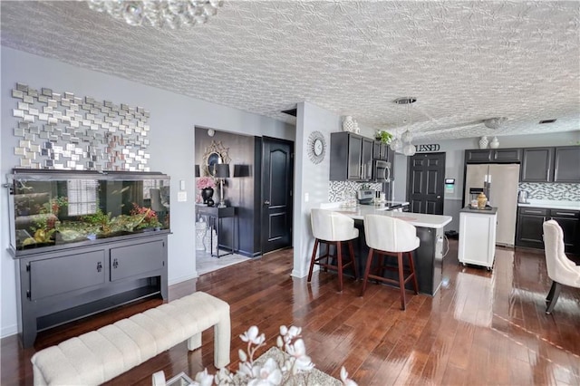 kitchen with appliances with stainless steel finishes, dark hardwood / wood-style floors, gray cabinetry, backsplash, and a kitchen bar