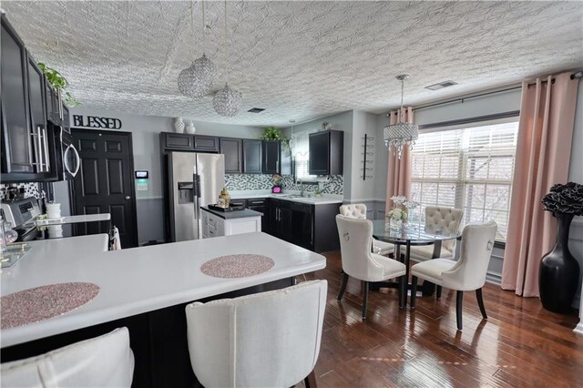 kitchen featuring pendant lighting, dark wood-type flooring, appliances with stainless steel finishes, decorative backsplash, and kitchen peninsula