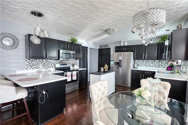 kitchen with sink, dark wood-type flooring, appliances with stainless steel finishes, a kitchen breakfast bar, and decorative light fixtures