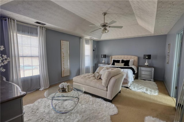 carpeted bedroom with ceiling fan, a tray ceiling, and a textured ceiling