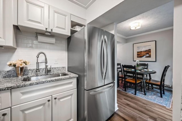 kitchen featuring freestanding refrigerator, a sink, ornamental molding, dark wood-style floors, and white cabinetry