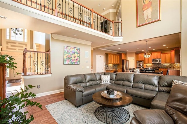 living room featuring crown molding, light wood finished floors, an inviting chandelier, baseboards, and stairs