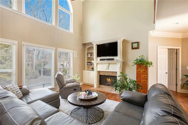 living room with a fireplace with flush hearth, wood finished floors, baseboards, built in features, and ornamental molding