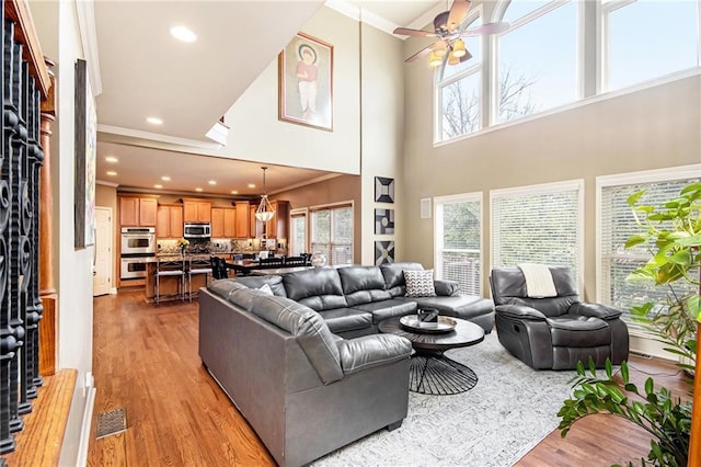 living area featuring ornamental molding, light wood-type flooring, plenty of natural light, and a ceiling fan