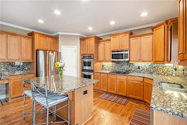 kitchen featuring a center island, a breakfast bar area, stainless steel appliances, light wood-style floors, and a sink