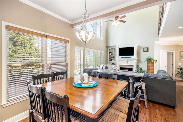 dining room with ornamental molding, a lit fireplace, baseboards, and wood finished floors