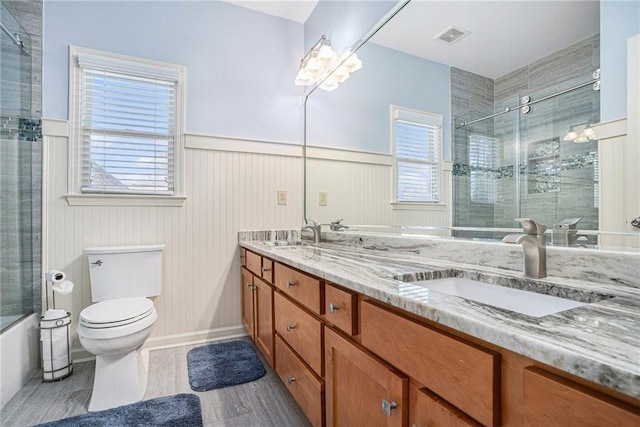 full bathroom featuring toilet, a wainscoted wall, a sink, visible vents, and a tile shower